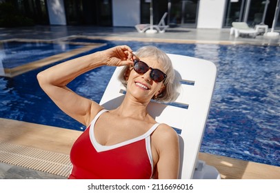 Happy Vacation. Senior Woman In Red Swimwear On The Sunlounger Near The Swimming Pool.