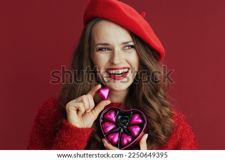 Happy Valentine. smiling trendy 40 years old woman in red sweater and beret with heart shaped candy box.