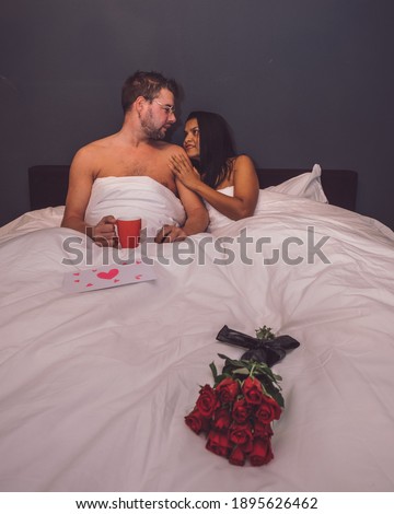Happy valentine's couple, mid-age Asian woman with European man with red roses and a love letter on Valentine day 14 February, couple in bed with red roses and valentine card