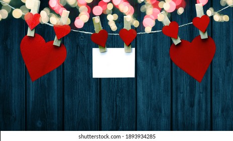 Happy Valentine's Day Background - Red Hearts And White Paper Note Hang On Wooden Clothes Pegs With Wooden Heart And Bokeh Lights On A String Isolated On Blue Wooden Wall, With Space For Text