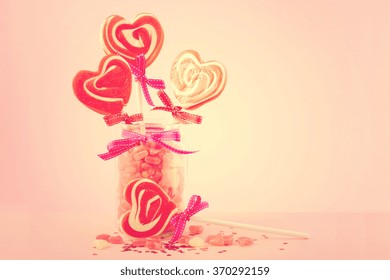 Happy Valentines Day candy with red heart shape lollipops on pink wood background with copy space and applied retro vintage style filters.