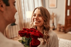 Happy Valentine's Day. A Man Gives A Bouquet Of Red Roses To His Beloved Woman In The Living Room Of The House. Romantic Evening Together.