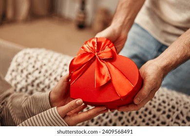 Happy Valentine's Day. A man gives a heart-shaped gift box to his beloved woman in the living room at home. Romantic evening together. - Powered by Shutterstock