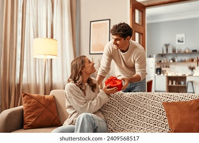 Happy Valentine's Day. A man gives a heart-shaped gift box to his beloved woman in the living room at home. Romantic evening together. - Powered by Shutterstock