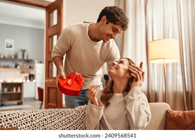 Happy Valentine's Day. A man gives a heart-shaped gift box to his beloved woman in the living room at home. Romantic evening together. - Powered by Shutterstock