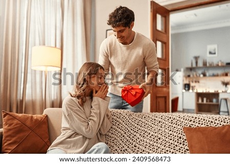 Happy Valentine's Day. A man gives a heart-shaped gift box to his beloved woman in the living room at home. Romantic evening together.