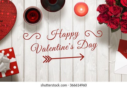 Happy Valentines Day scene with gift, wine, candle, roses, envelope on wooden table.