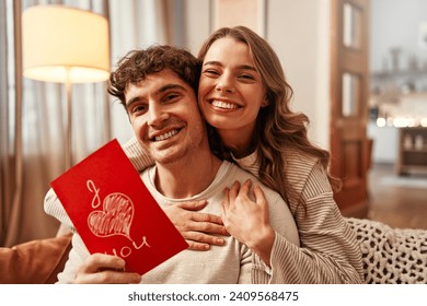 Happy Valentine's Day. A woman gives a greeting card to her beloved man with the inscription I love you in the living room at home.