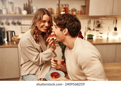 Happy Valentine's Day. Young couple in love eating cakes while sitting on the table in the kitchen, romantically spending the evening together. - Powered by Shutterstock