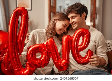 Happy Valentine's Day. Young couple in love holding a balloon with the inscription love while sitting on the sofa in the living room at home. Romantic evening together.