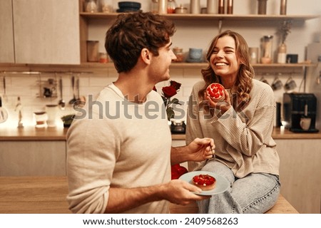 Happy Valentine's Day. Young couple in love eating cakes while sitting on the table in the kitchen, romantically spending the evening together.