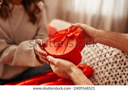 Happy Valentine's Day. Young couple in love exchanging gifts while sitting on the sofa in the living room at home. A man giving a heart-shaped gift box to his beloved woman. Photo stock © 