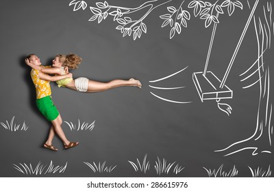 Happy valentines love story concept romantic couple against chalk drawings background  Male catching his girlfriend jumping from tree swings 