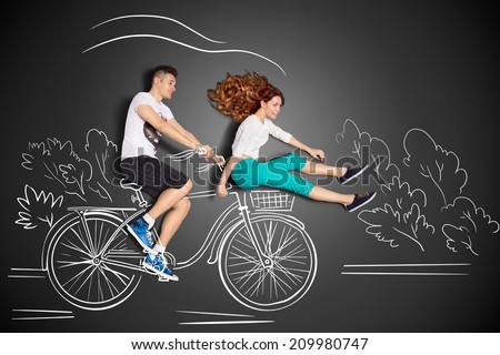 Happy valentines love story concept of a romantic couple against chalk drawings background. Male riding his girlfriend in a front bicycle basket.
