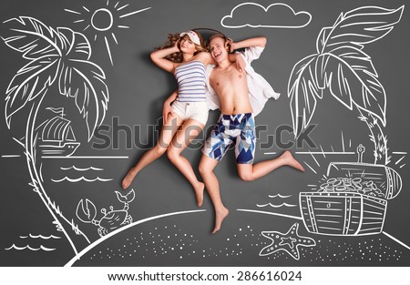 Happy valentines love story concept of a romantic couple on a desert island, sharing headphones, and listening to the music against chalk drawings background of a sea and a treasure chest.