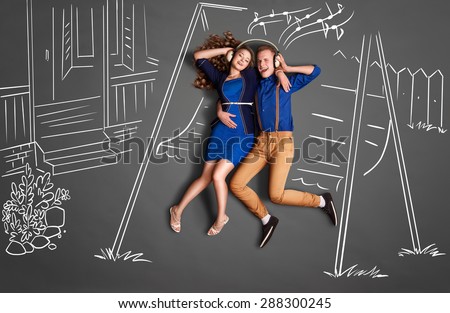 Happy valentines love story concept of a romantic couple sitting on the canopy swing sharing headphones and listening to the music against chalk drawings backyard background.