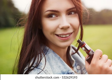 Happy Vaper Girl With Vaping Device In Hand.Quit Smoking Nicotine Cigarettes,start Vaporizing.Tasty Fruit Flavor E-liquid,vape E-juice.Attractive Young Woman Vaping Ecig.Vaper Girl With Happy Smile