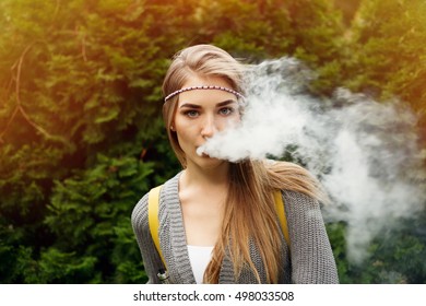 Happy vaping young white blonde girl.Smiling female model smoking fruit flavored e-liquid or e-juice with vaporizer device or e-cig.Modern gadget for smokers