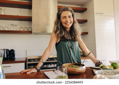 Happy vegan woman smiling at the camera while preparing a plant-based meal. Mature woman following an organic recipe in her kitchen. Healthy senior woman eating clean at home. - Powered by Shutterstock