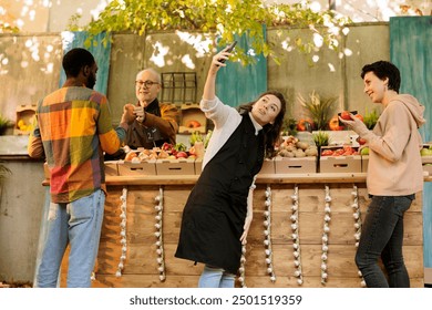 Happy vendor poses for selfie with female customer in front of farmers market stand filled with fresh, locally grown fruits and vegetables. Making use of social media to promote small business market. - Powered by Shutterstock