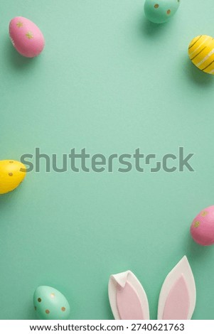 Happy vertical Easter greeting concept featuring pastel decorated eggs and bunny ears arranged as a border on a mint green background perfect for celebration cards and seasonal spring designs