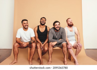 Happy Vibes In The Studio. Four Body Positive Men Laughing Cheerfully While Sitting On A Bench. Group Of Self-confident Young Men Feeling Comfortable In Their Natural Bodies.