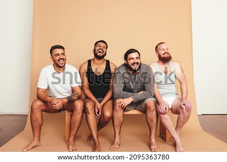 Happy vibes in the studio. Four body positive men laughing cheerfully while sitting on a bench. Group of self-confident young men feeling comfortable in their natural bodies.