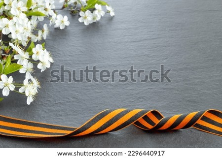 Happy Victory Day! May 9 Russian Victory Day. St. George ribbon with bouquet of sakura branch on  black granite monument with empty space for text.  Flat lay creative mockup