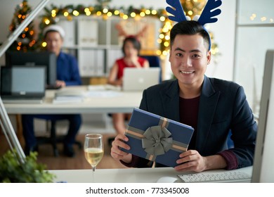 Happy Vietnamese businessman with Christmas present sitting at his table - Shutterstock ID 773345008
