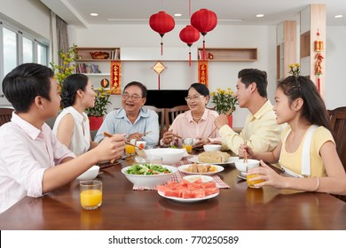 Happy Vietnamese family celebrating Tet at home; couplets with best wishes for the upcoming year in the background