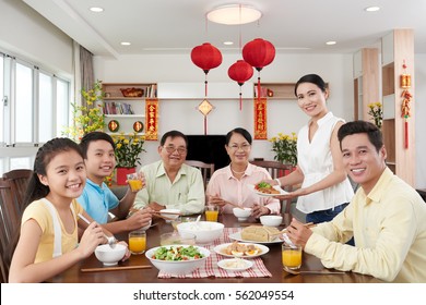 Happy Vietnamese family having dinner for Tet celebration; couplets with best wishes for coming year in the background