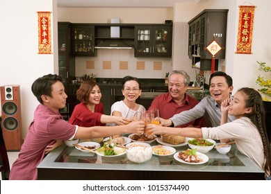 Happy Vietnamese family toasting with glasses of juice. Scrolls wishing luck and wealth in the background