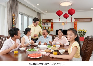 Happy Vietnamese little girl enjoying New Year dinner with family; couplets with best wishes for coming year in the background