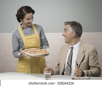 Happy vintage couple having dinner, she is serving a pizza to her husband