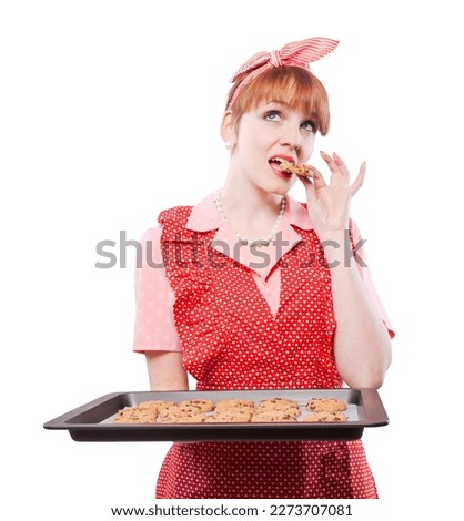Happy vintage style housewife tasting her freshly baked homemade sweets, she is holding a baking tray full of cookies