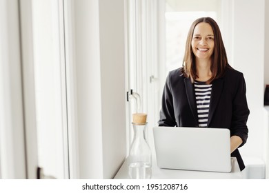 Happy Vivacious Businesswoman With A Genuine Welcoming Smile Seated Working At A Laptop Computer In A High Key Office With Copyspace Looking At The Camera