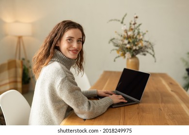 Happy Vivacious Young Woman With An Engaging Smile Pausing From Working On Her Laptop At An Office Table To Turn And Look At The Camera