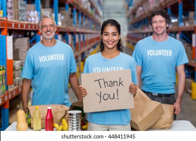 Happy volunteer holding a sign and posing with her team in a warehouse