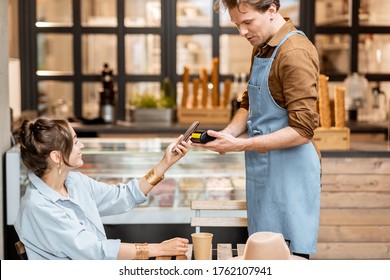 Happy waiter with a client at the cafe or ice-cream shop, making contactless payment with a smartphone - Powered by Shutterstock