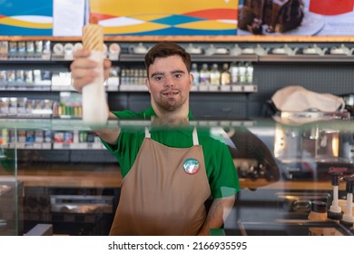 Happy Waiter With Down Syndrome Standing By Counter And Giving Sandwich To A Costumer In Cafe At Gas Station.