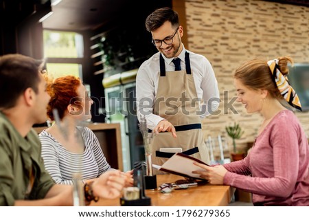 Happy waiter having fun while talking to his guests and taking order from them in a cafe, 