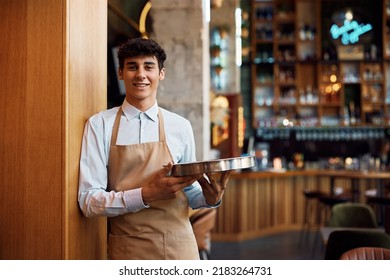 Happy waiter holding a tray while working in cafe and looking at camera.