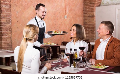 Happy Waiter Placing Order In Front Of Guests In Country Restaurant