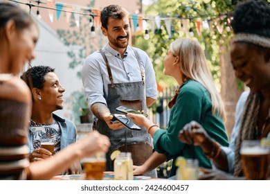 Happy waiter receiving smart phone contactless payment form a woman who is being with her friends in a cafe.  - Powered by Shutterstock