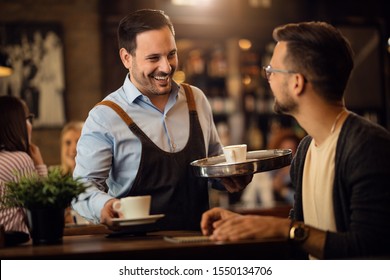 Happy waiter serving coffee and communicating with male guest in a bar.  - Powered by Shutterstock