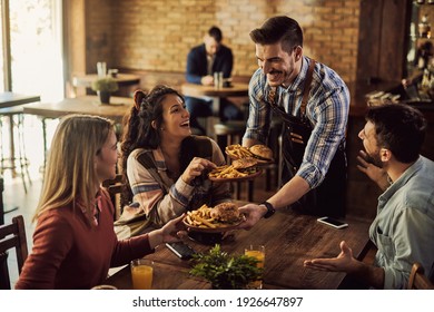Happy waiter serving hamburgers with French fries to customers in a pub. 
