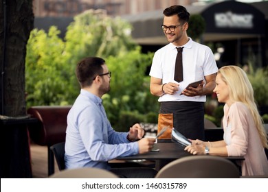 Happy waiter using digital tablet while talking to a couple and taking order from them in a restaurant.  - Powered by Shutterstock