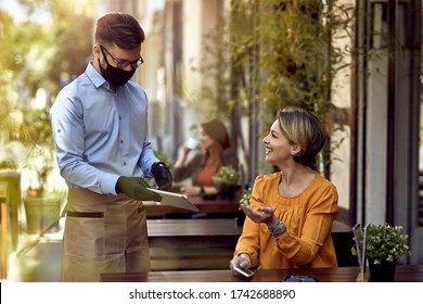 Happy waiter wearing protective face mask while showing menu on digital tablet to female guest in a cafe.  - Powered by Shutterstock