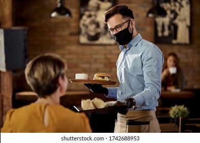 Happy waiter wearing protective face mask and gloves while bringing food to a customer in a pub.  - Powered by Shutterstock