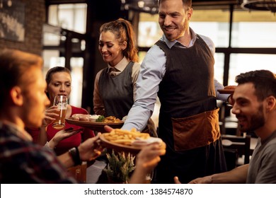 Счастливые официанты приносят еду за стол и обслуживают группу друзей в ресторане.
